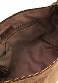 Interno di una borsa in tessuto marrone con texture liscia, chiusura a zip e multiple tasche, tra cui un compartimento con zip e un'etichetta del marchio.