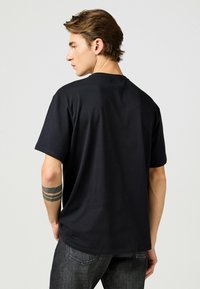 Sort bomulds T-shirt med korte ærmer, rund hals og en afslappet pasform. Synlige sting langs kanten og ærmerne.