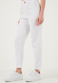 Valged denim-püksid elastse vöökohtaga, mis sisaldavad esist nuppu ja on kitsas lõikega. Kombineeritud valgete tossekingadega, et luua lõdvestunud välimus.