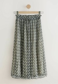 Jupe mi-longue plissée avec taille élastique et motif géométrique noir et blanc suspendue sur un cintre en bois.