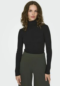 Maglione a collo alto nero in tessuto a coste, con maniche lunghe e una forma aderente, abbinato a pantaloni oliva a vita alta.
