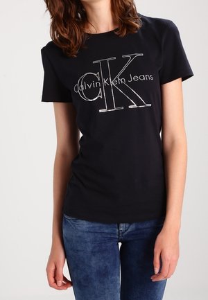 Zwart katoenen T-shirt met een groot wit "CK" logo en de tekst "Calvin Klein Jeans". Getailleerd ontwerp met korte mouwen en een ronde hals.