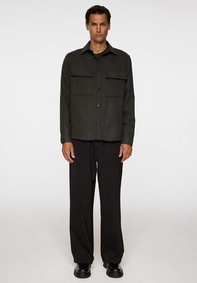 Mörkgrön kn�äppt skjorta med två bröstfickor, krage, mjuk textur. Matchad med lösa svarta byxor och robusta svarta skor.