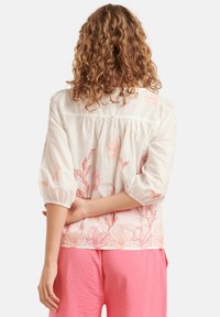 Lichte stoffen shirt met pofmouwen, versierd met roze bloemenpatronen op een beige achtergrond. Gecombineerd met roze gestructureerde broeken.