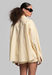 Geel en wit gestreepte oversized shirt met lange mouwen, knoopmanchetten en achterafdruk; gladde, lichte stof.