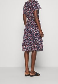 Sukienka w kwiaty w granatowym kolorze z czerwonymi i białymi kwiatami, krótkie rękawy, falbaniasty dół, lekka tkanina, połączona z prostymi czarnymi klapkami.