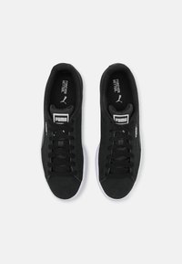 Černé semišové tenisky s bílými gumovými podrážkami, černými tkaničkami, logem Puma na jazyku a boku a hladkým, minimalistickým designem.