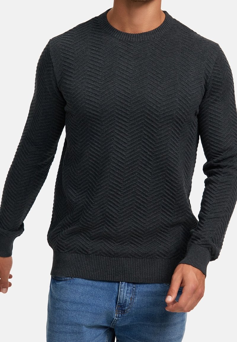Ciemnoszary sweter z dzianiny z teksturowanym wzorem w jodełkę, okrągłym dekoltem oraz ściągaczami na mankietach i u dołu. Zestawiony z niebieskimi dżinsami.