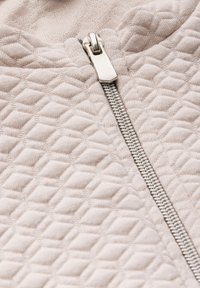 Béžová zipová bunda s texturovaným vzorem vystouplých diamantů a stříbrným kovovým zipem, s jemnými švy.