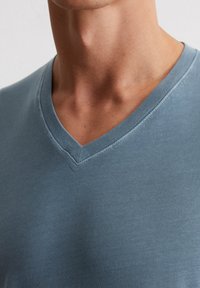 T-shirt col en V en coton bleu discret, avec une texture lisse et un col côtelé, offrant une coupe décontractée et des finitions de couture minimales.