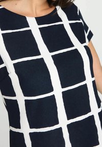 Námořnická košile s bílou mřížkovanou vzorovou, krátkými rukávy, kulatým výstřihem, hladkým povrchem a přesnými mřížkovými liniemi tvořícími čtvercové tvary.
