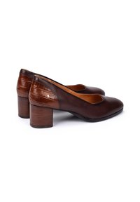 Une paire de chaussures en cuir marron foncé à talons bloc, avec un panneau arrière texturé et un bout arrondi, photographiée sur fond blanc.