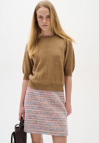 Brun stickad kortärmad tröja i kombination med en flerfärgad texturerad minikjol med vågiga mönster. Modellen håller en mörk handväska.