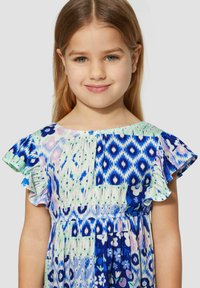 Bunt gefesseltes Kleid mit gemischten blauen Mustern, kurzen rüschierten Ärmeln, gerafftem Taillenzug und floralen Akzenten auf hellem Hintergrund.