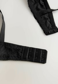 Svarta spets- och tygbh-band med justerbara krokar och spetskant. Har en slät yta med intrikata spetsdetaljer.