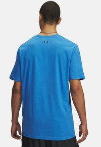 Camiseta de algodón azul con corte relajado, mangas cortas y cuello redondo. Presenta una pequeña impresión de logo en la parte superior de la espalda.