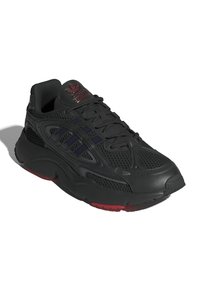 Scarpa sportiva nera con rivestimento in rete e sintetico, parte superiore testurizzata, colletto imbottito alla caviglia, dettagli rossi posteriori e design a tre strisce.