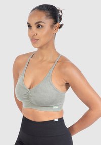 Vihreä ribattu urheiluliivi, jossa on V-kaulasuunnittelu ja säädettävät ohuet hihnat, yhdistettynä korkeavyötäröisiin mustiin legginsseihin.