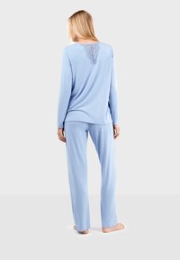 Ensemble de pyjama bleu clair comprenant des manches longues et un pantalon. Le dos présente des détails en dentelle intriqués. Tissu doux avec une coupe décontractée.