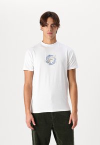 Witte katoenen t-shirt met een grafische print in het blauw, met een ronde halslijn en korte mouwen, gecombineerd met groene kordonbroek.
