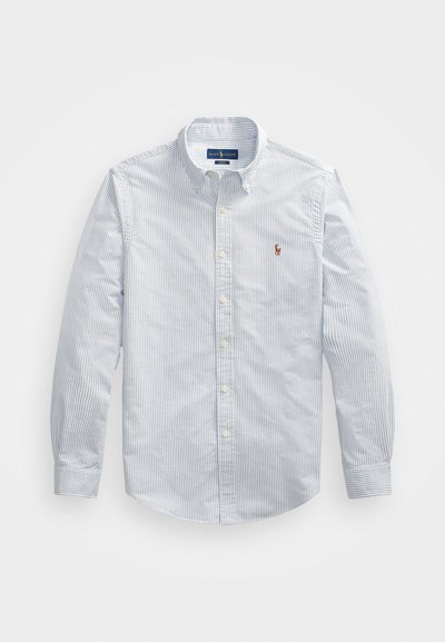 Lyseblå og hvit stripete skjorte med knapper, lange ermer, spiss krage og en liten brodert logo på brystet.