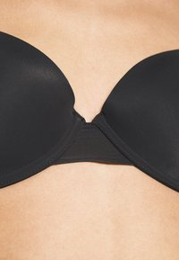Black strapless bra with smooth, ribbed fabric. Features molded cups and a wide band for support, showcased against skin tone.