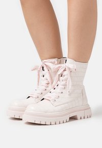 Bottes blanches en cuir verni à cheville avec une texture crocodile, dotées de lacets roses, d'une fermeture éclair latérale et d'une semelle blanche épaisse.