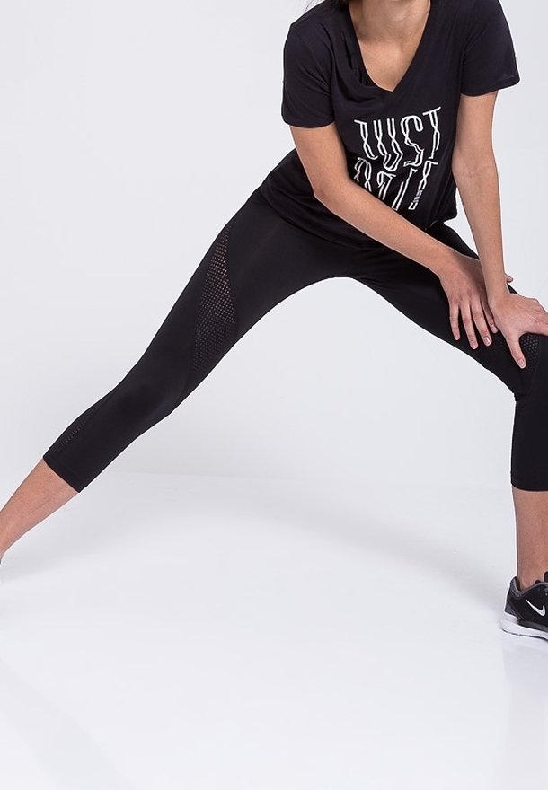 Mallas deportivas negras con paneles de malla a los lados, combinadas con una camiseta negra holgada con texto blanco. Zapatillas deportivas grises.