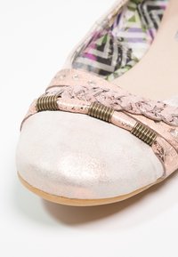 Chaussure plate rose texturée avec un embout argenté brillant, ornée d'accents tressés et de ferrures métalliques. L'intérieur est doublé d'un tissu à motifs géométriques.