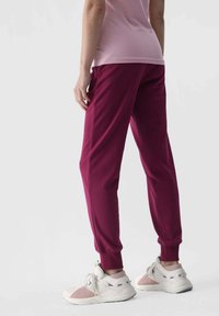 Bordeauxfarbene Jogginghosen mit gerippten Bündchen, elastischem Bund und seitlichen Taschen, kombiniert mit hellen Sneakers mit Pastellakzenten.