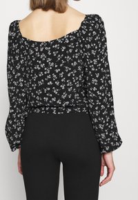 Blusa nera a fiori con schiena a scollo, maniche lunghe a palloncino e motivi floreali bianchi; abbinata a leggings neri.