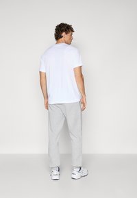 White short-sleeve t-shirt and gray sweatpants worn by a person from the back, displaying simple design and relaxed fit. White sneakers complete the look.