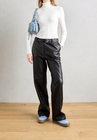 Kobieta w białym, długim swetrze z golfem, czarnych skórzanych spodniach z paskiem, jasnoniebieskich sneakersach i pasującej jasnoniebieskiej torebce na ramię.