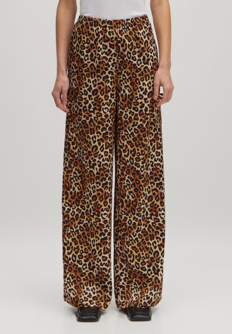 Leopardprint wijdere broeken gemaakt van zachte stof, met een elastische tailleband en levendige oranje, zwarte en tan kleuren.