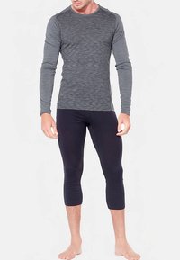 Top sportivo grigio a maniche lunghe con motivo a onde testurizzate, abbinato a leggings neri corti. Entrambi gli indumenti sono aderenti ed elasticizzati.