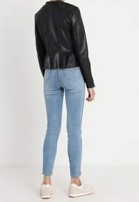 Zwarte leren peplumjack met een aansluitend ontwerp, gecombineerd met lichtblauwe skinny jeans en witte sneakers, gezien van achteren.