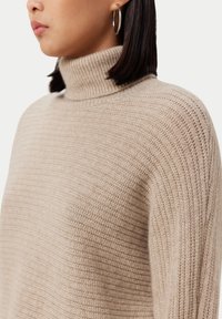 Beige ribbad polokrage tröja med en avslappnad passform. Har ett strukturerat stickat mönster och en hög krage som ger värme.