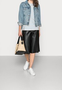 Jeansjacke, gestreiftes weiß-blaues Oberteil, schwarze Kunstleder-Culottes, weiße Sneakers und eine beigefarbene geflochtene Tasche mit schwarzen Akzenten.