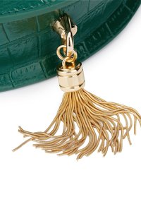 Breloque pompon en métal doré attachée à un coin de sac en cuir vert texturé.