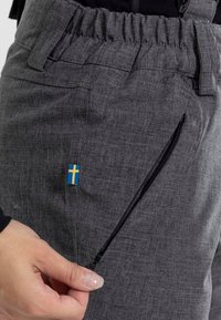 Grå tekniska byxor med elastisk midja, sidoficka med dragkedja och en liten svensk flagga som detalj. Materialet har ett strukturerat mönster.