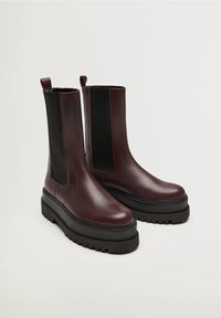 Bottines en cuir bordeaux avec des panneaux latéraux élastiques noirs, bout rond et semelle en caoutchouc noir épais ; dotées de languettes pour un enfilage facile.