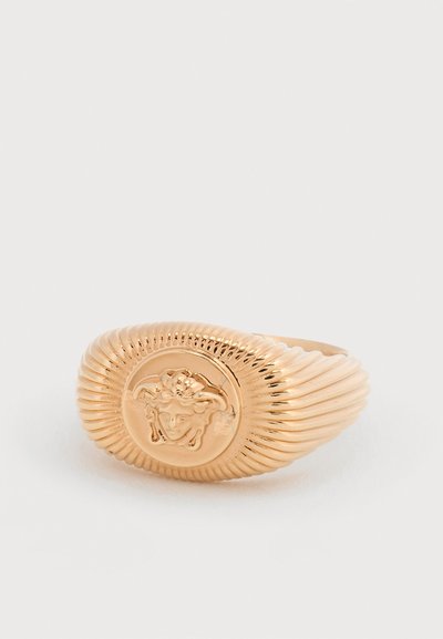 Δαχτυλίδι σινέτ από χρυσό τόνο με πλευρές ραβδωτές που εμφανίζουν ανάγλυφο έμβλημα κεφαλής Μέδουσας σε λείο κυκλικό πρόσωπο.