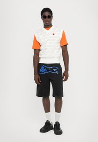 Hvid og orange kortærmet top med teksten "ICECREAM", sorte denimshorts med en blå grafik, og sorte sneakers med hvide sokker.
