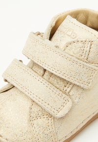 Beige, met glitter bedekte peuterschoen met twee klittenbandbandjes. Gemaakt van zacht materiaal, met een ronde neus en gestikte details.