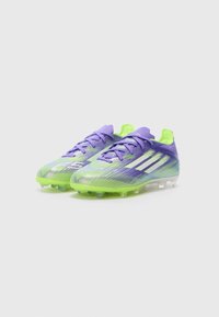 Paarse en fluorescerend groene voetbalschoenen hebben een textuur op de bovenkant, een vetersluiting en doorzichtige noppen voor grip op grasoppervlakken.