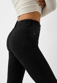 Vaqueros negros de denim, con un diseño ajustado, cintura alta, dos bolsillos traseros y detalles de costura sutiles.