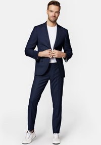 Granatowy garnitur w kratę o slim fit i z klapami, połączony z białym t-shirtem i białymi sneakersami. Dopasowane spodnie i detale z guzikami.