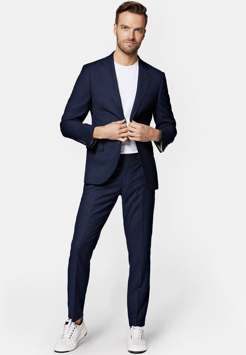 Granatowy garnitur w kratę o slim fit i z klapami, połączony z białym t-shirtem i białymi sneakersami. Dopasowane spodnie i detale z guzikami.