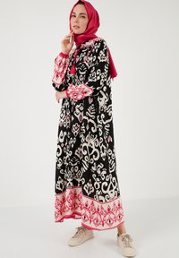 Black maxi dress with contrasting white and pink abstract patterns. Features long sleeves, a round neckline, and a pink hemline. Worn with beige sneakers.
