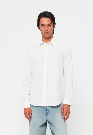 White long-sleeve shirt featuring a subtle texture, button placket, and classic collar, paired with light blue denim jeans.